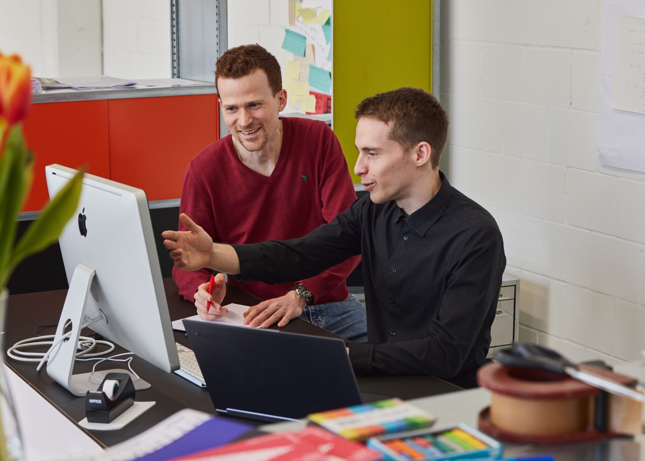 Bruno explaining something on a laptop to a colleague at a desk