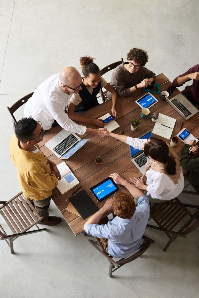 Group at a meeting table with laptops, 2 people shaking hands