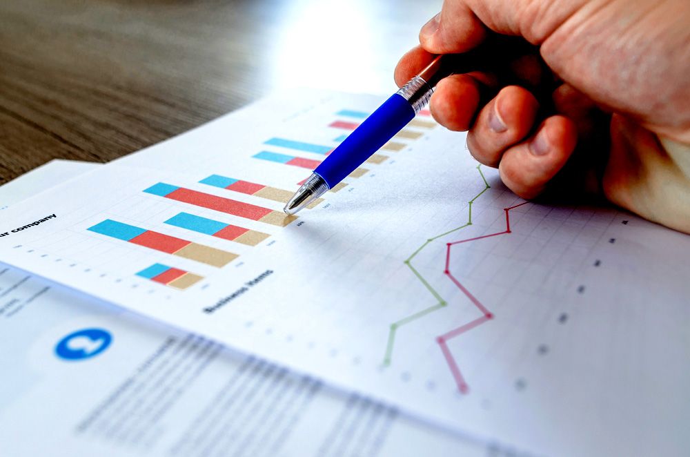 Hand with a ballpoint pen over a printout with bar and line charts
