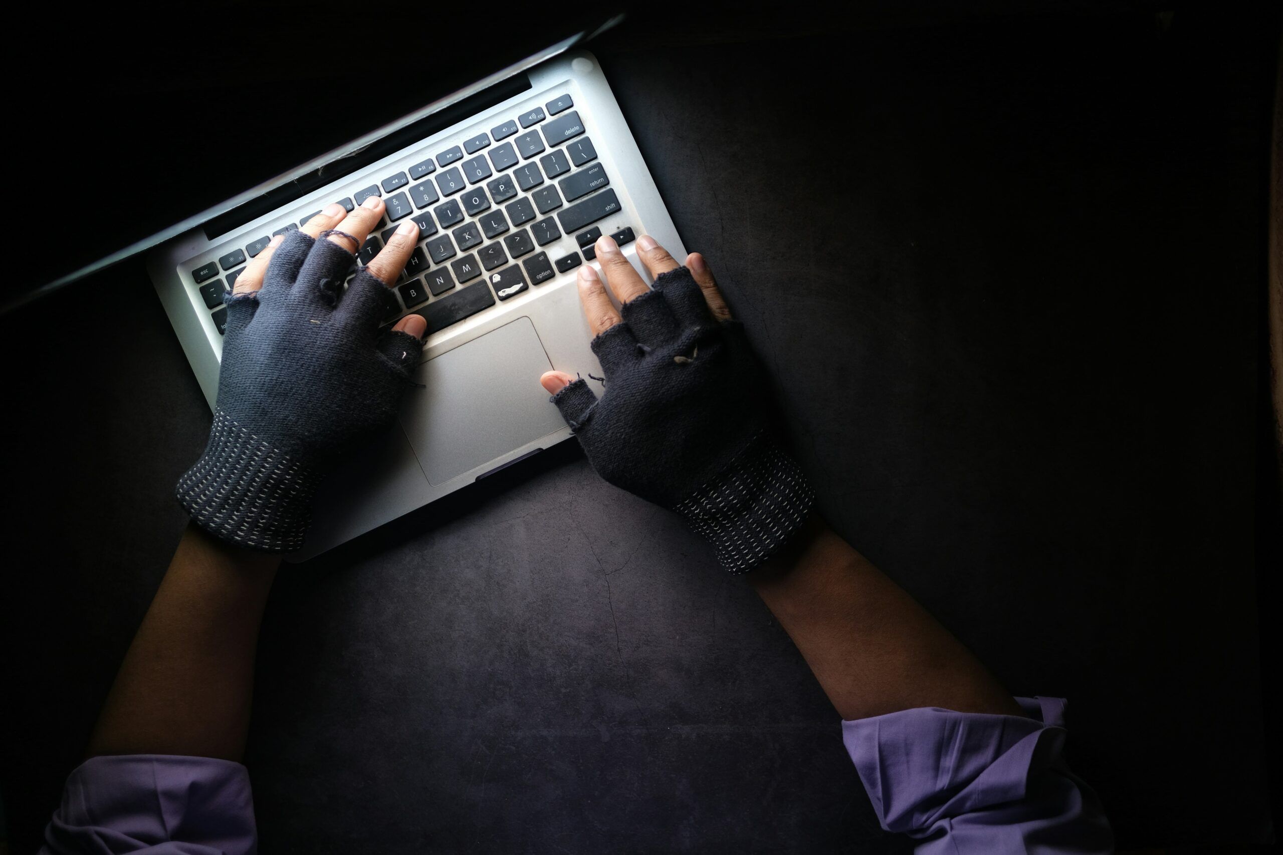 Gloved hands typing on a laptop keyboard in the dark