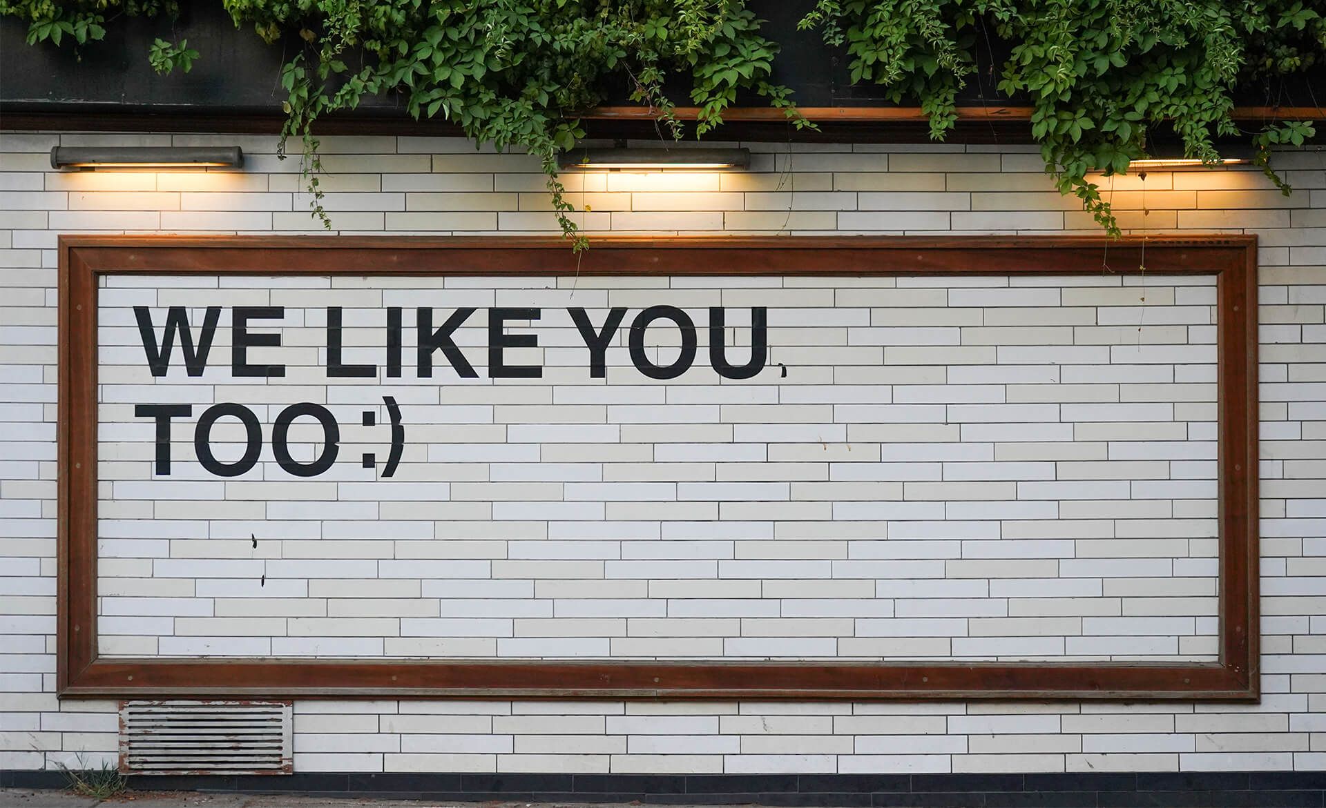 Sign on a brick wall reading «We like you too :)»