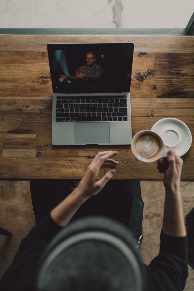 Person at a wooden table with a coffee cup following a video conference on a laptop